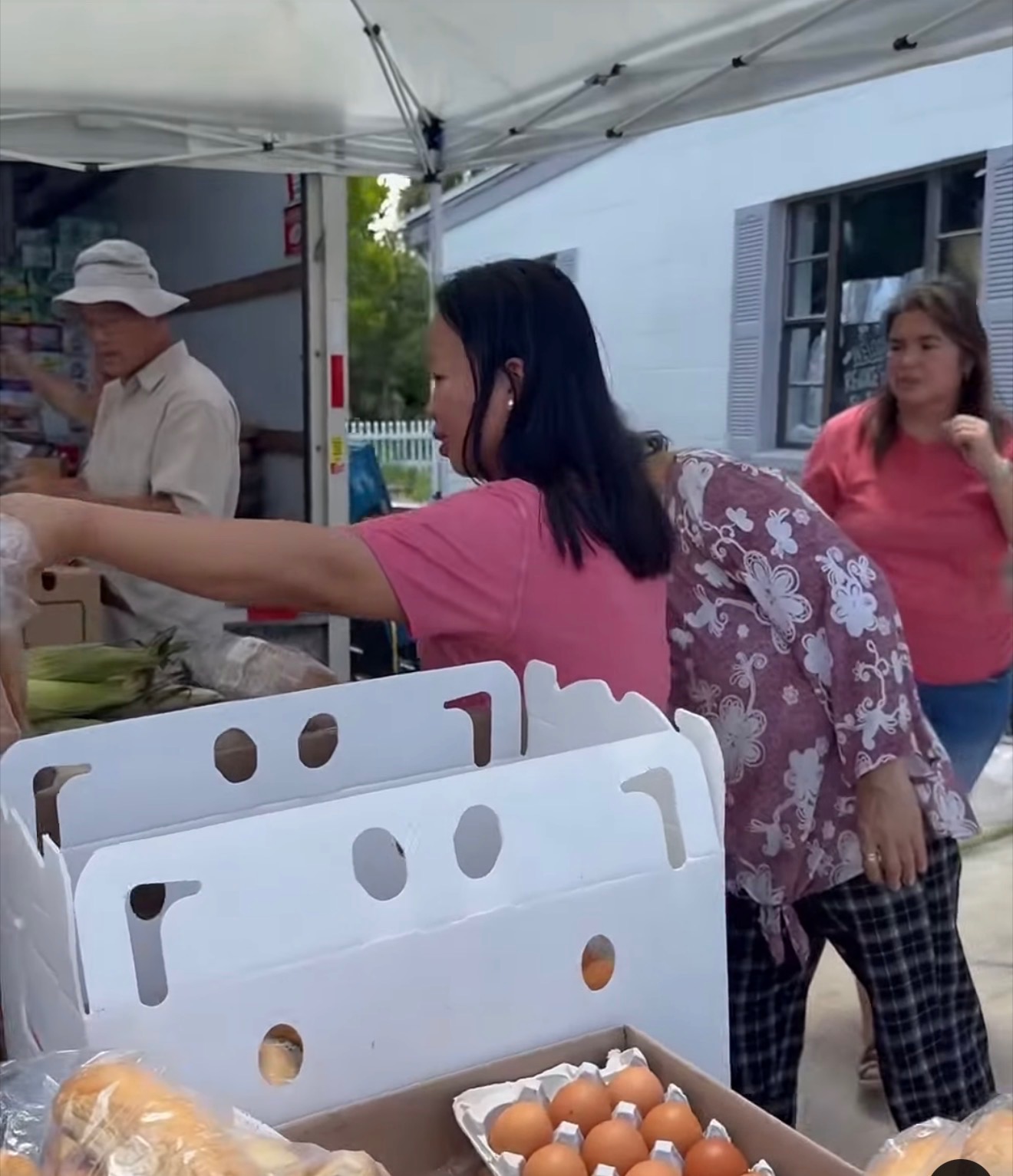 A volunteer at a market stand with fresh produce and eggs for neighbors